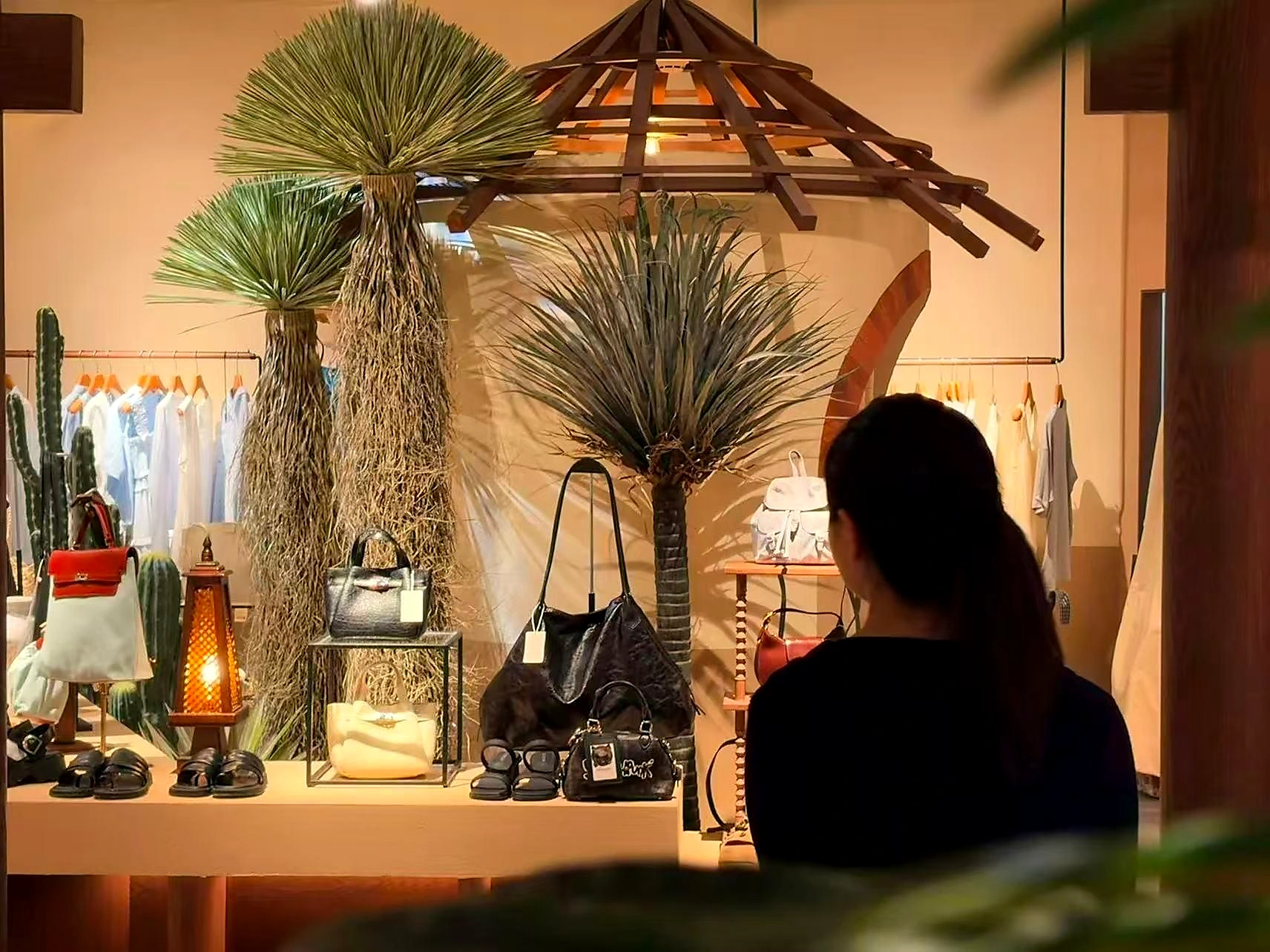 植物、木质吊灯、包袋和服饰组成的橱窗场景